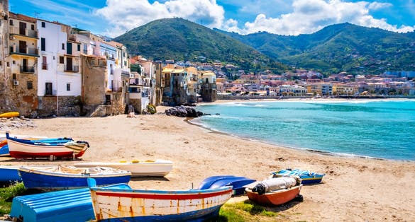 Fishing boats on beach of Cefalu, medieval town on Sicily island, Italy. Seashore village with historic buildings, clear turquoise sea water and mountains. Popular tourist attraction near Palermo.