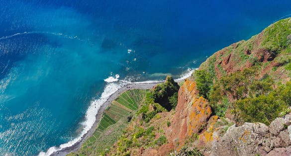 View down from the 'Miradouro do Cabo Girão' viewpoint, Câmara de Lobos. Blue Atlantic ocean and rocky coast with green agricultural fields. Beautiful volcanic landscape of Madeira island, Portugal.
