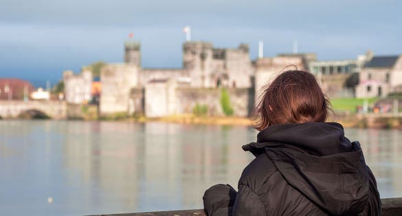 photo of Young teenager girl looking at stunning King John's stone castle with tall walls and towers. Limerick city, Ireland. Travel and sightseeing concept. Selective focus. .