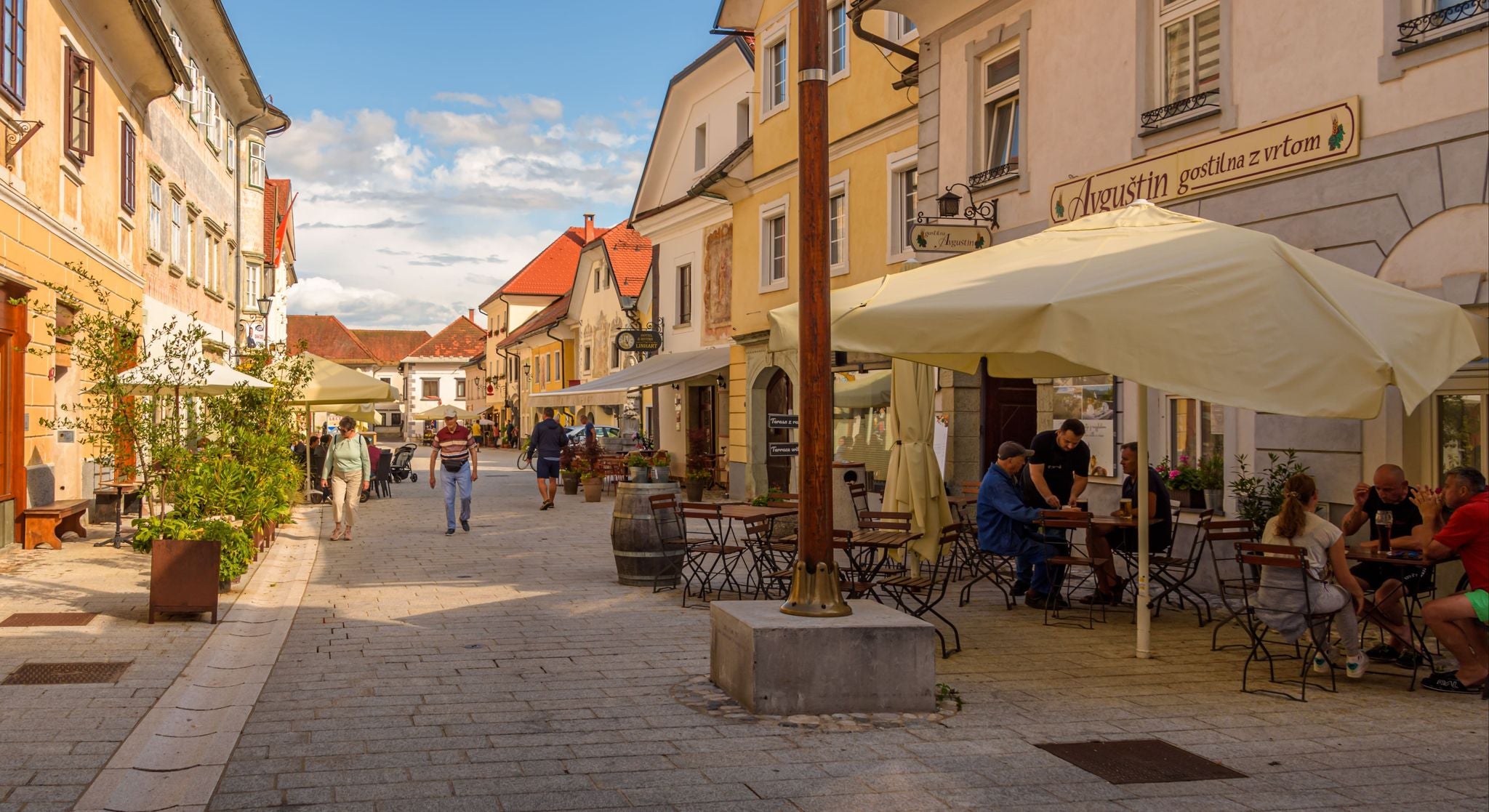 People dining and walking along a charming cobblestone street lined with cafés in Radovljica, Slovenia..jpg
