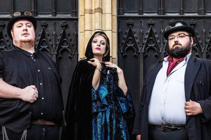 Three people in steampunk and gothic-style clothing pose in front of a dark, ornate metal gate with serious expressions..jpg