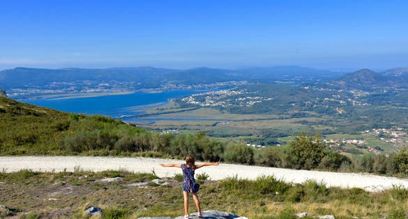 Happy young girl with her hands raised up stands on the edge of the cliff against the backdrop of a beautiful view of the sea. Viewpont. Portugal. Santo Antaо. Caminha. Viana do Castelo.