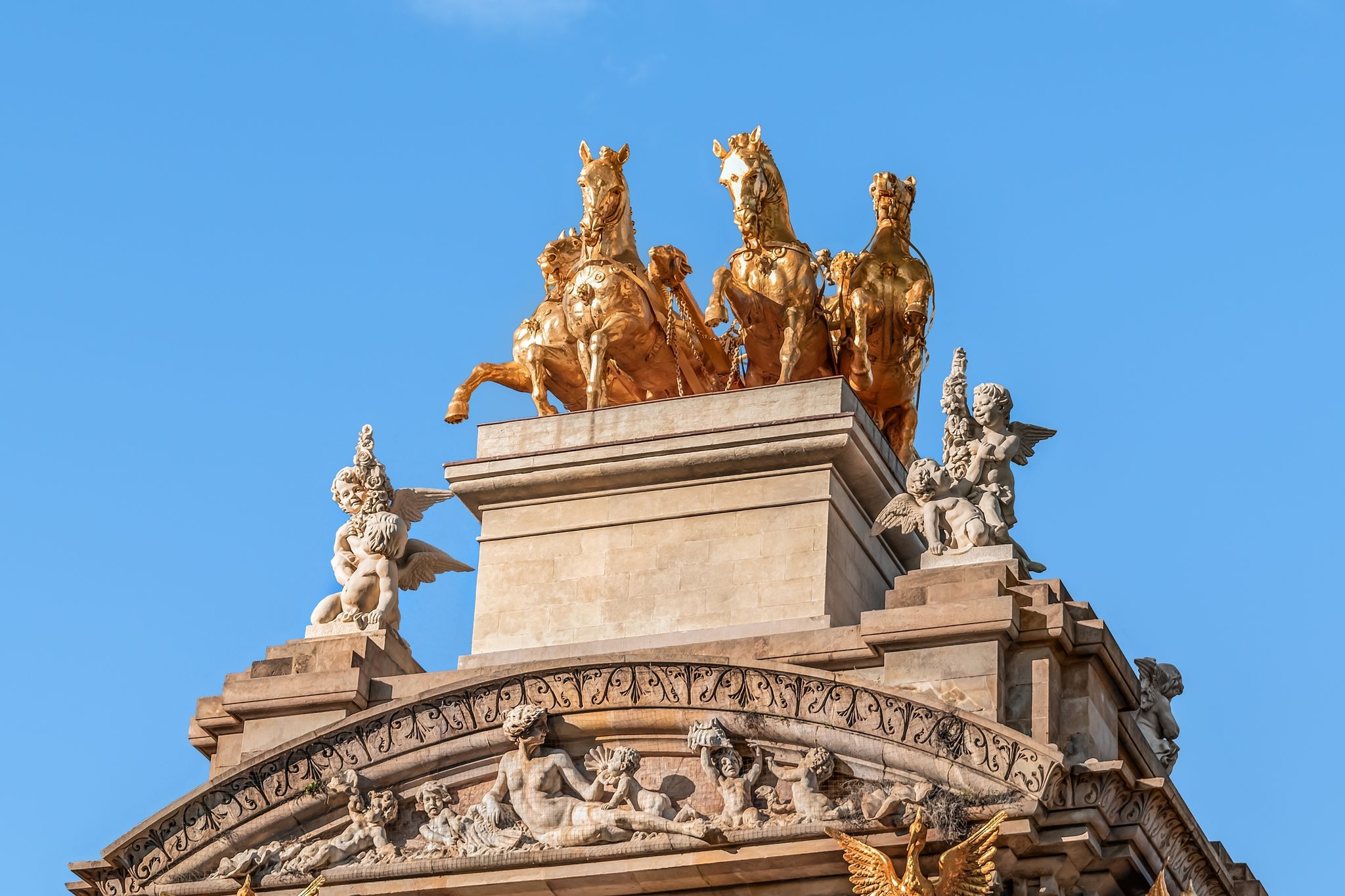 Photo of sculptures of angels and a golden horses from Aurora Quadriga on the top of the Font de la Cascade in Barcelona, Spain.
