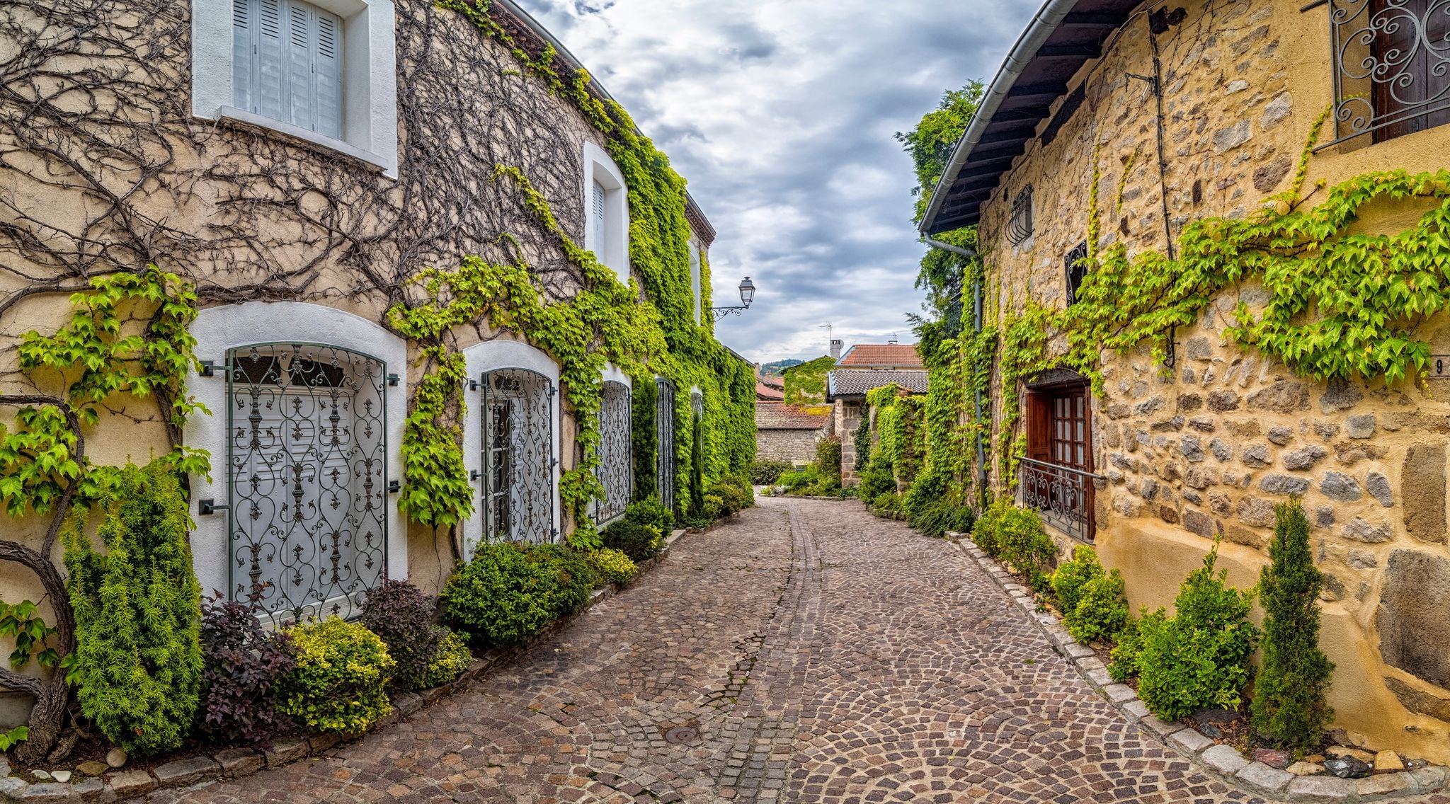 Photo of A narrow street lined with stone buildings covered in lush greenery in Saint-Etienne ,France.