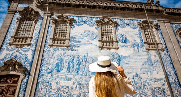Photo of young woman tourist standing near the church with famous Portuguese blue ceramic tiles on the facade in Porto city, Portugal.