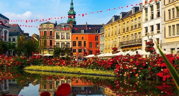Picturesque summer view of flowering central Grand Place square in Mons overlooking baroque belfry of Roman Catholic Church of St. Elizabeth towering over colorful residential townhouses, Belgium