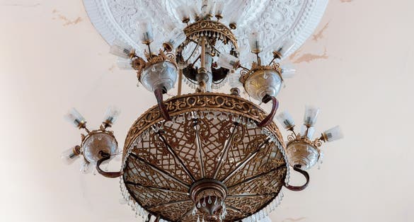 Old style vintage brass crystal chandelier in Niko Berdzenishvili Kutaisi State History Museum, main exhibition room, gypsum ornaments on the ceiling.
