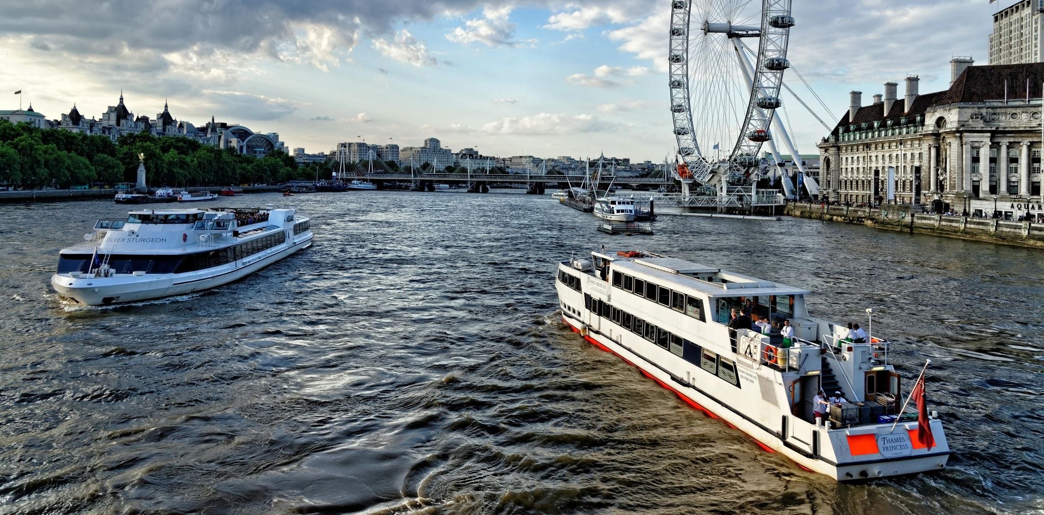 Thames River cruise boats sailing past the London Eye during golden hour..jpg