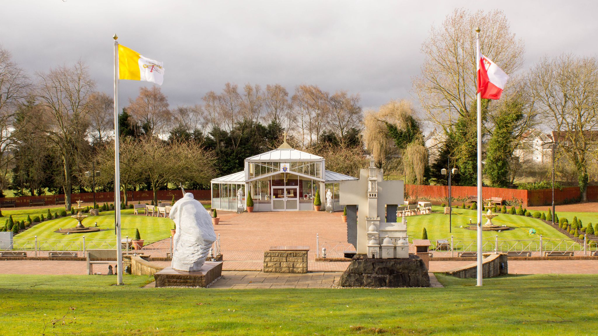 Photo of Look at the Park in Grotto, in Carfin, Scotland. Photo Showing Vatican Flag on Left, Polish Flag at Right and Glass Chapel at the Back.