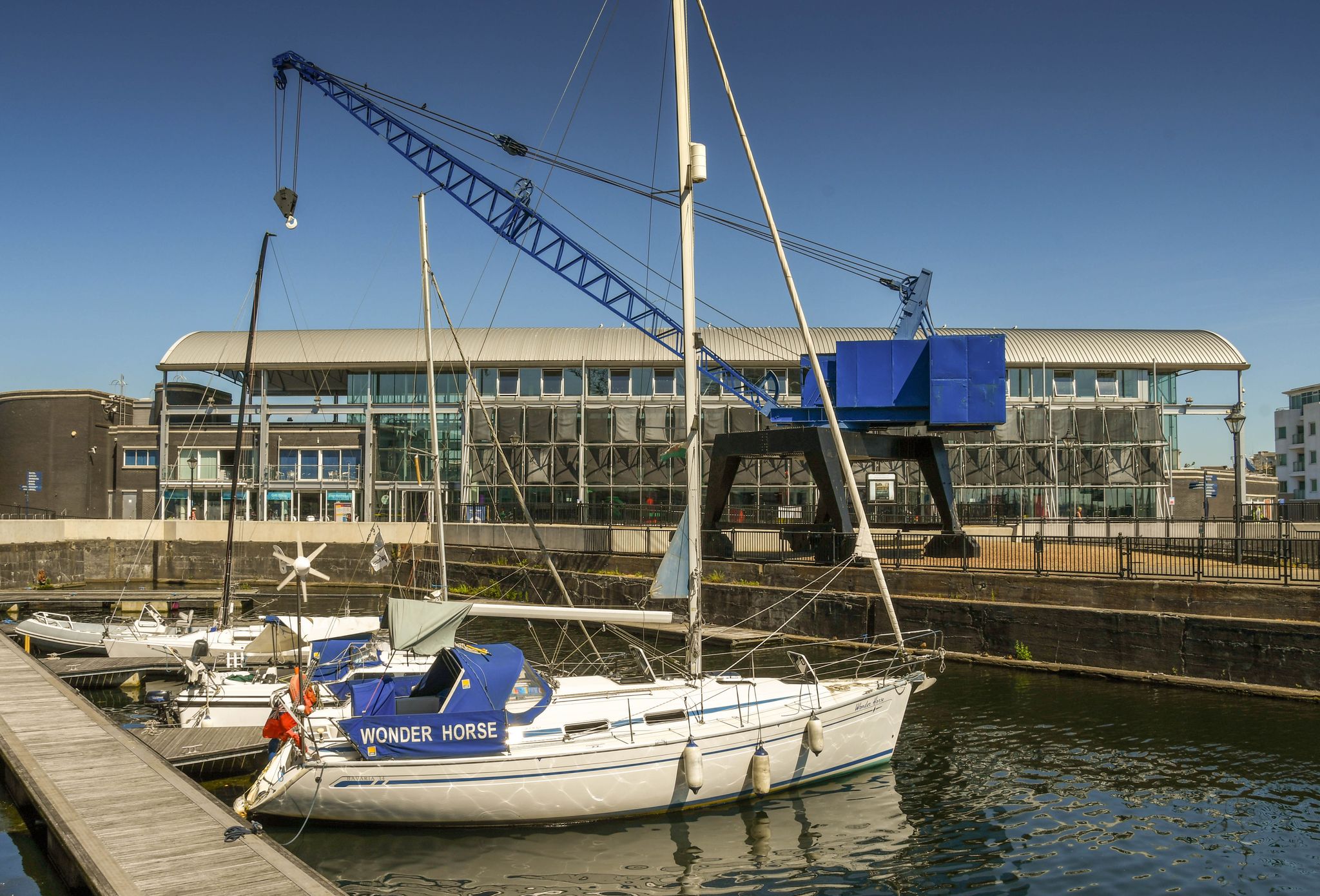  Sailing boat alongside a jetty in a restored dock in Cardiff Bay. In the background is the Techniquest building, a science and discovery learning centre.
