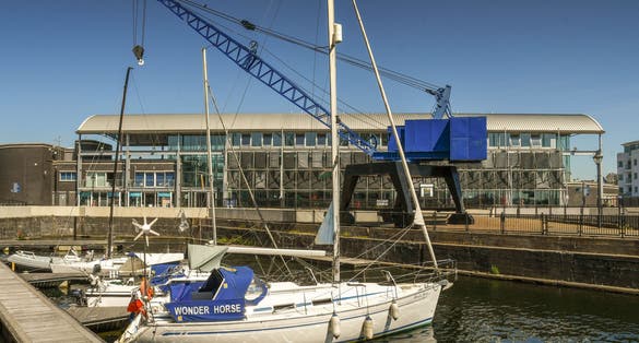  Sailing boat alongside a jetty in a restored dock in Cardiff Bay. In the background is the Techniquest building, a science and discovery learning centre.
