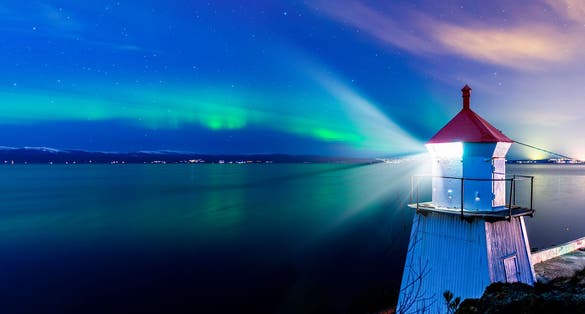 A light house in Trondheim with a sky with northern lights in the background.
