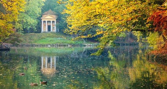 photo of Reflection of a little temple in a pond of the Park of Monza surrounded by yellow autumnal trees, Italy