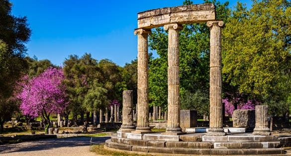 Photo of The ruins of Ancient Olympia with blooming cercis tree. Greece.