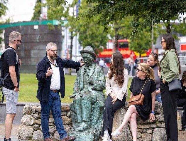A tour guide talks to a group of people sitting near a bronze statue of a man in a public park in Galway..jpg