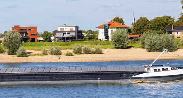 Cityscape of Nijmegen in The Netherlands with scenic view on cargo boats passing the bridge in river Waal on a sunny autumn day.