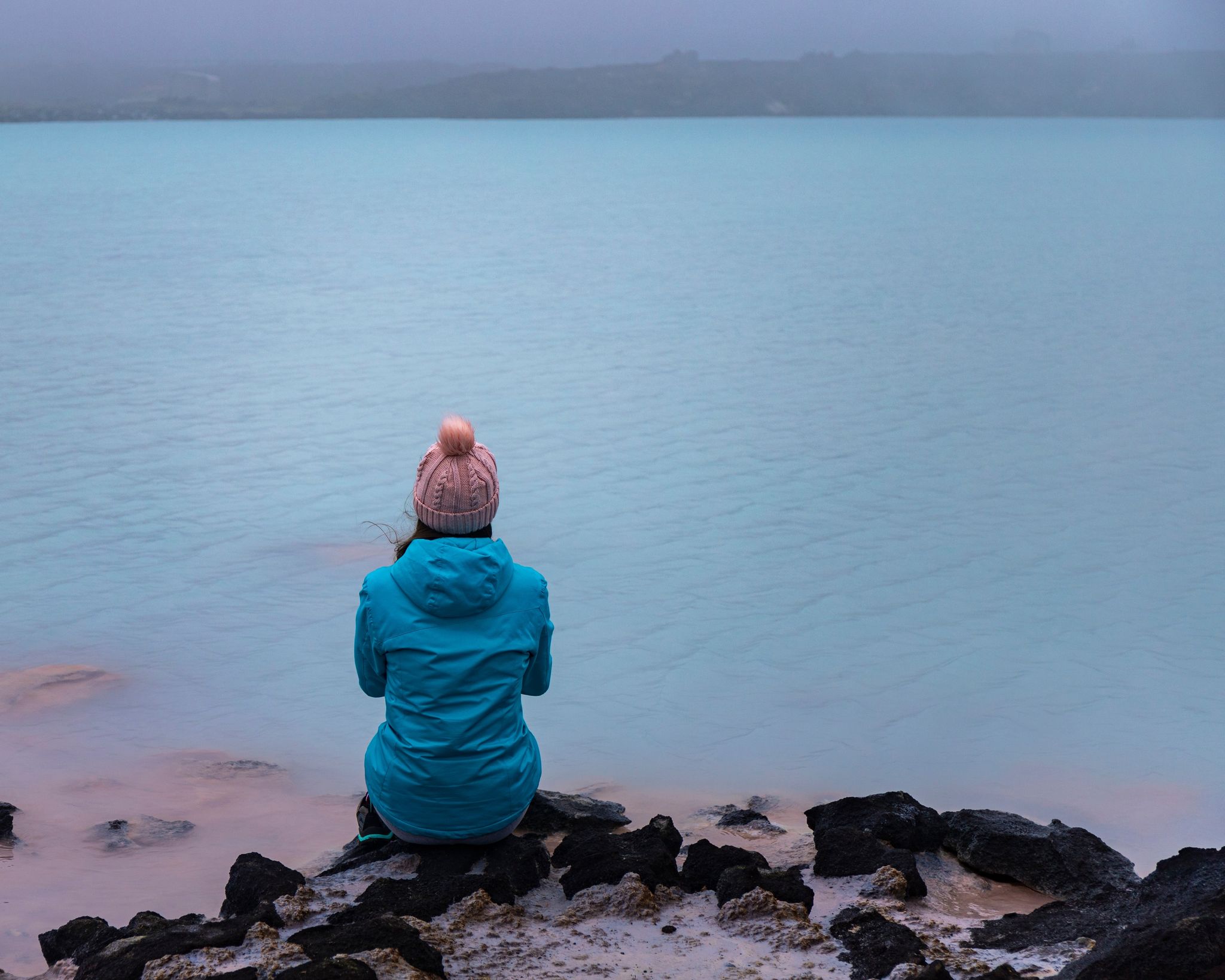 photo of Girl in blue jacket sits on the rocks and admires stunning blue colored lagoon near Gunnuhver Hot Springs. Hidden gems of Iceland .
