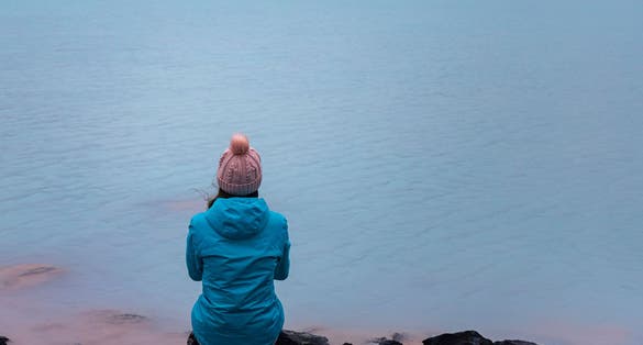 photo of Girl in blue jacket sits on the rocks and admires stunning blue colored lagoon near Gunnuhver Hot Springs. Hidden gems of Iceland .