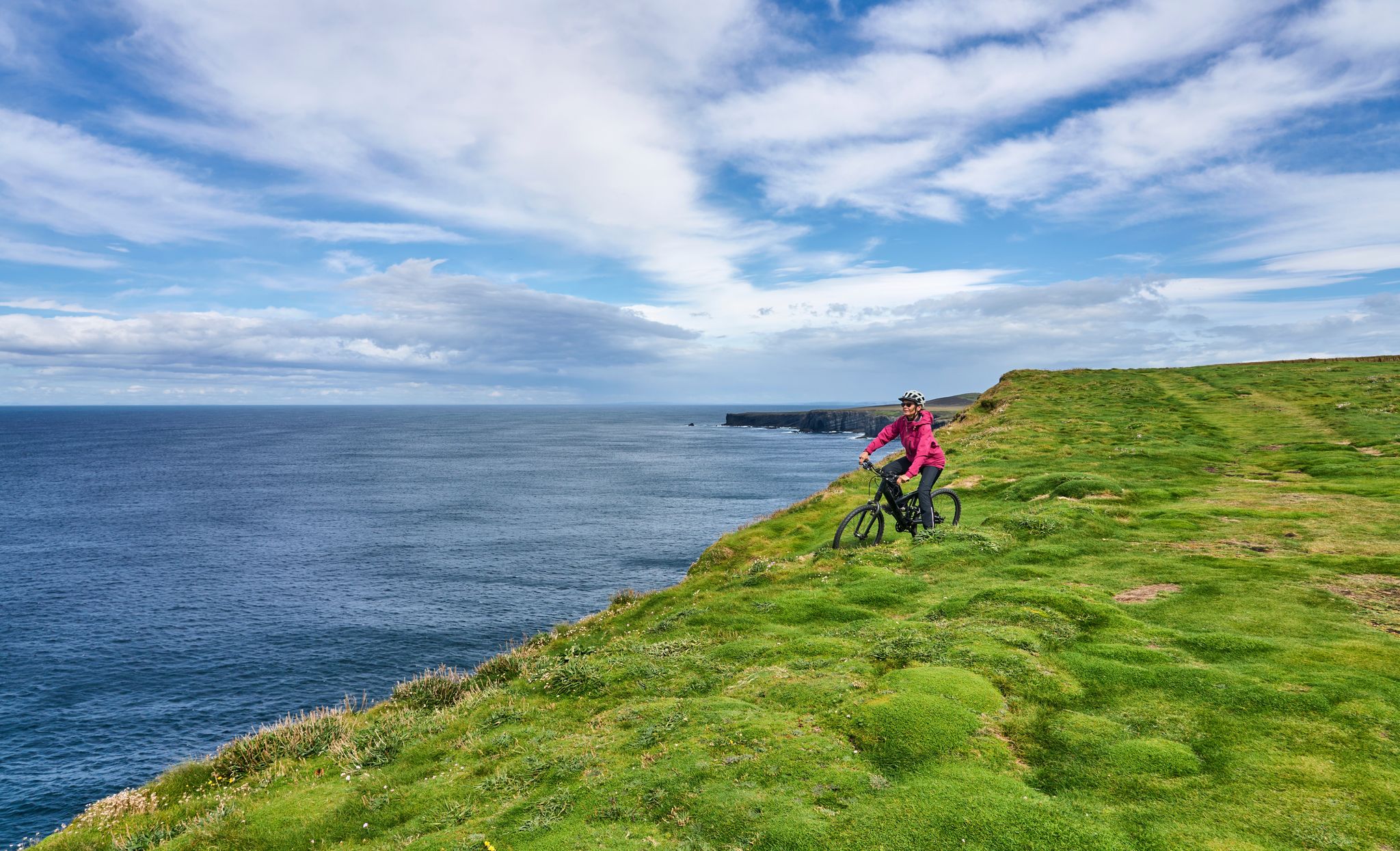 nice senior woman on mountain bike, cycling on the cliffs of Dunmore Head near Kilballyowen , County Limerick in the southwestern part of the Republik of Ireland
