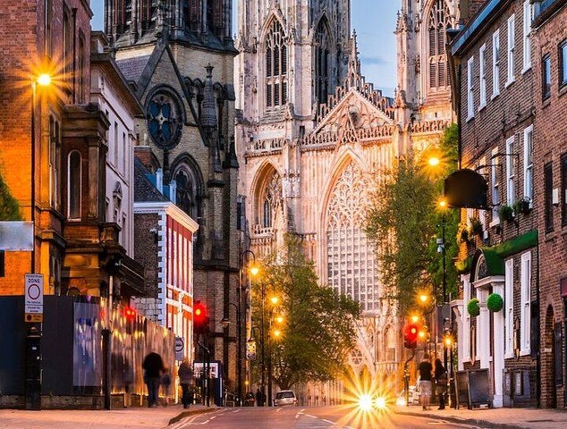 A view of York Minster-s grand facade at dusk, framed by city buildings and glowing streetlights..jpg