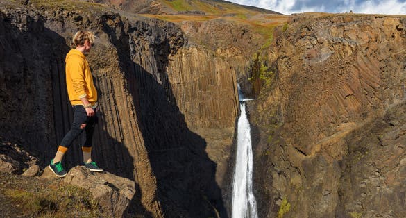 photo of Young hiker standing at the Litlanesfoss waterfall in Iceland. 