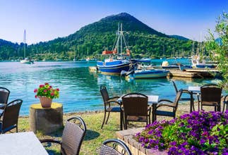 Photo of Beautiful view over terrace near the beach with flowers on table in Nydri harbor, seaport of Lefkada, in Greece.