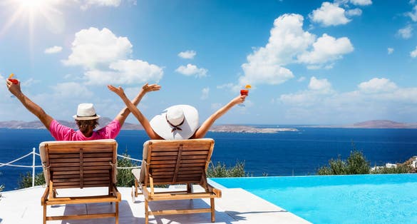 Photo of couple sitting on sunchairs enjoying the sun during their summer holidays in Mykonos.