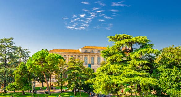 PHOTO OF Piazza Bra square in Verona city historical centre with park garden with green cedar and pine trees, Palazzo della Gran Guardia palace building, blue sky background, Veneto Region, Northern Italy