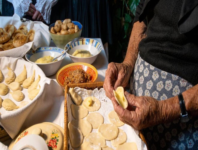 An elderly woman in Cagliari prepares traditional stuffed pasta by hand, surrounded by bowls of ingredients and pastries..jpg