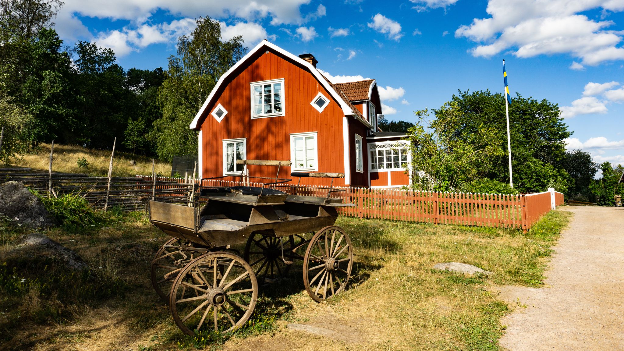 photo of old carriage in front of red wooden farming house on Katthult farmyard in Gibberyd, Sweden.
