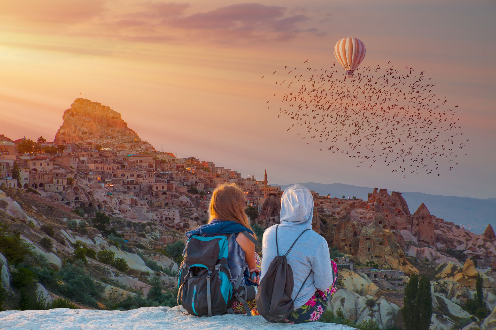 photo of girls watching beautiful sunset with hot air balloon over Pigeon Valley in Cappadocia, Turkey.
