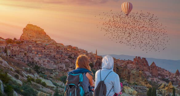 photo of girls watching beautiful sunset with hot air balloon over Pigeon Valley in Cappadocia, Turkey.