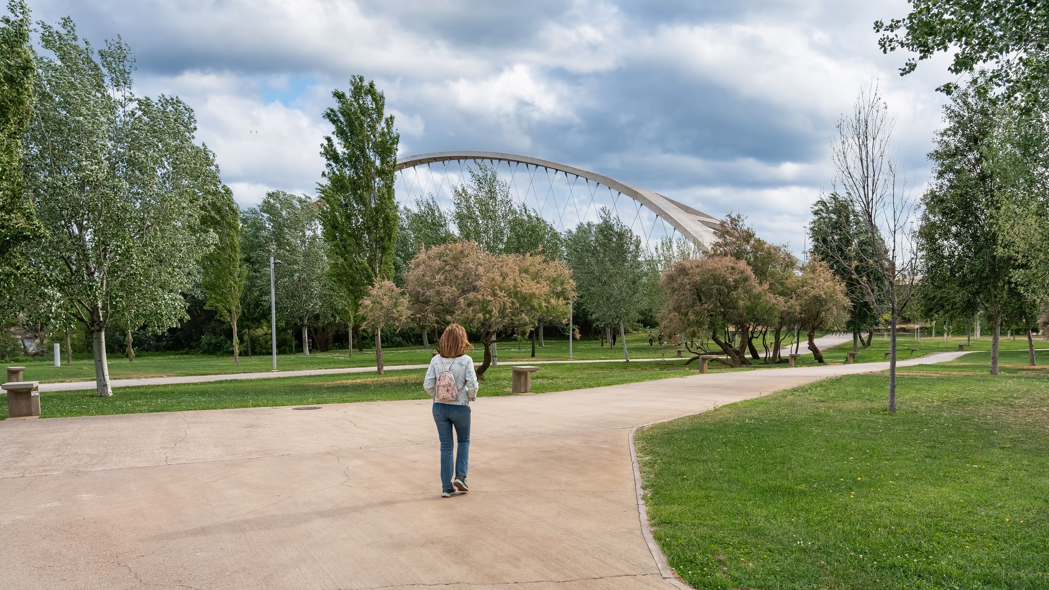 Photo of Woman with her back walking along the paths of the park next to the Ebro River in the city of Zaragoza, Spain.