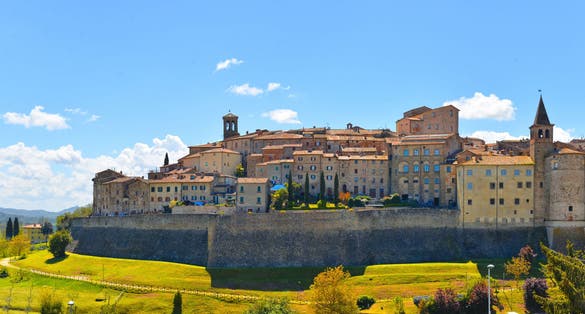 photo of view of landscape with Anghiari italian medieval village city walls on green hill and blue sky in background. Arezzo, Italy.