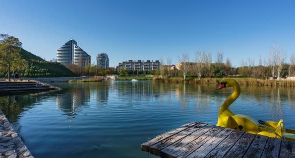 Photo of A lake inside Cabecera Park in Valencia city with buildings at background and a big yellow duck .