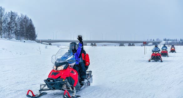 photo of people on snowmobile waving hand on the frozen lake in winter Rovaniemi, Lapland, Finland.