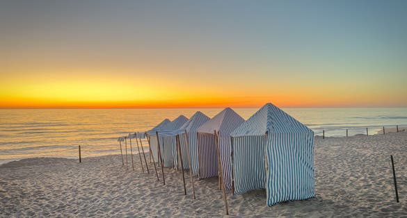 Photo of View of furadouro beach at sunset with blue and white striped beach tents. Ovar, Aveiro, Portugal.