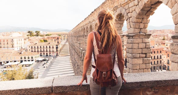 Photo of woman tourist enjoying view of Roman aqueduct on plaza del Azoguejo in Spain.