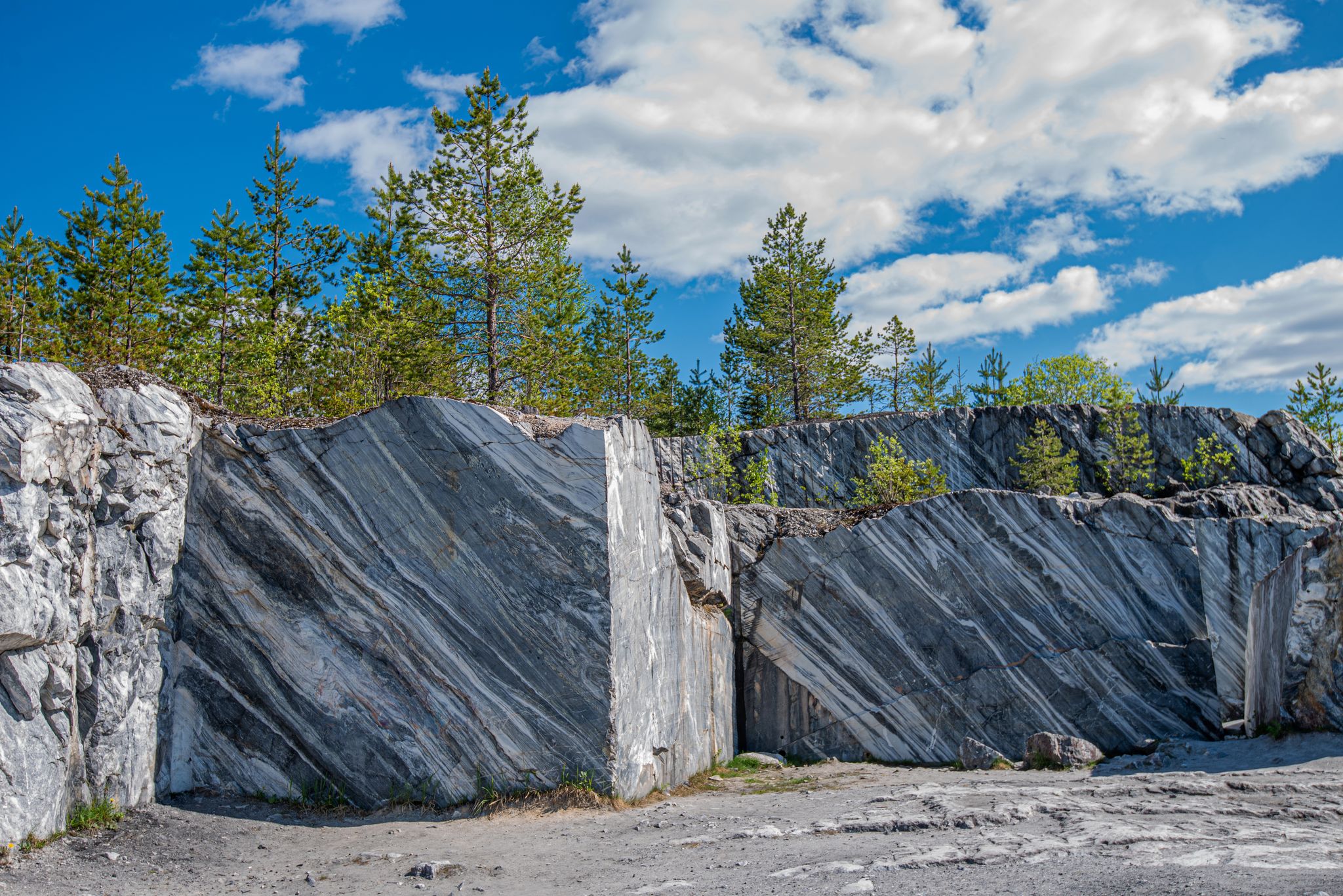 photo of Large grey stones in an old abandoned quarry. Marble texture. Smooth cuts on the rocks. The marble quarry is horizontal. The natural stone. Marble quarry, marble rocks in the wild.