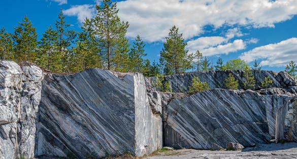 photo of Large grey stones in an old abandoned quarry. Marble texture. Smooth cuts on the rocks. The marble quarry is horizontal. The natural stone. Marble quarry, marble rocks in the wild.