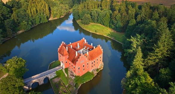 Photo of aerial view of bizarre water castle Cervena Lhota, red château standing at the middle of a lake on a rocky island, Czech Republic.