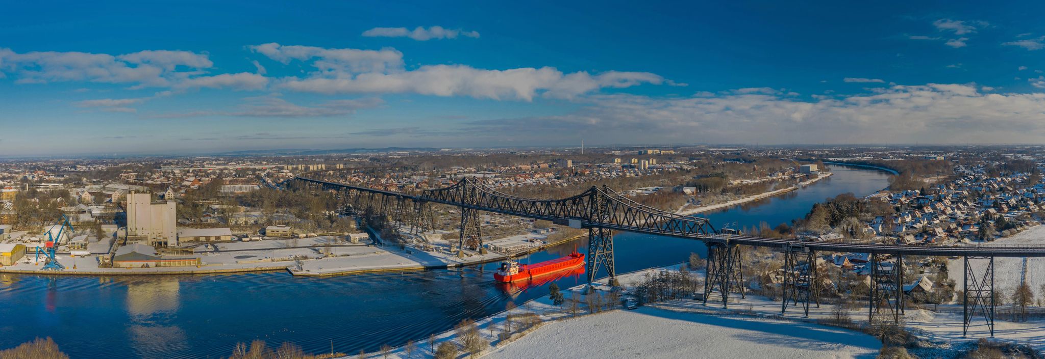 Panoramic aerial view of famous railway Rendsburg High Bridge with cargo ship with snow and frost in winter. panorama aerial view of port and city Rendsburg in winter with snow and frost.