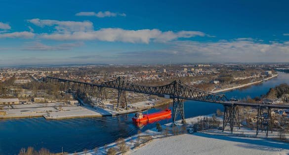 Panoramic aerial view of famous railway Rendsburg High Bridge with cargo ship with snow and frost in winter. panorama aerial view of port and city Rendsburg in winter with snow and frost.