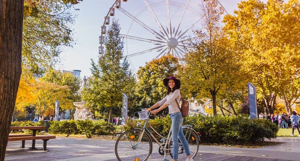 A happy young woman travel by bicycle and stop near the Budapest Eye big Ferris wheel in Budapest