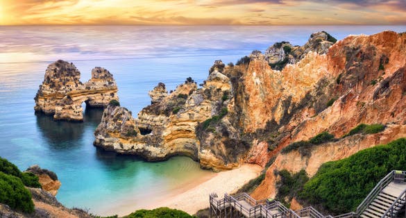 Photo of the beautiful Camilo beach in Lagos, Portugal, with its magnificent cliffs and the blue ocean colorfully lit at sunrise.