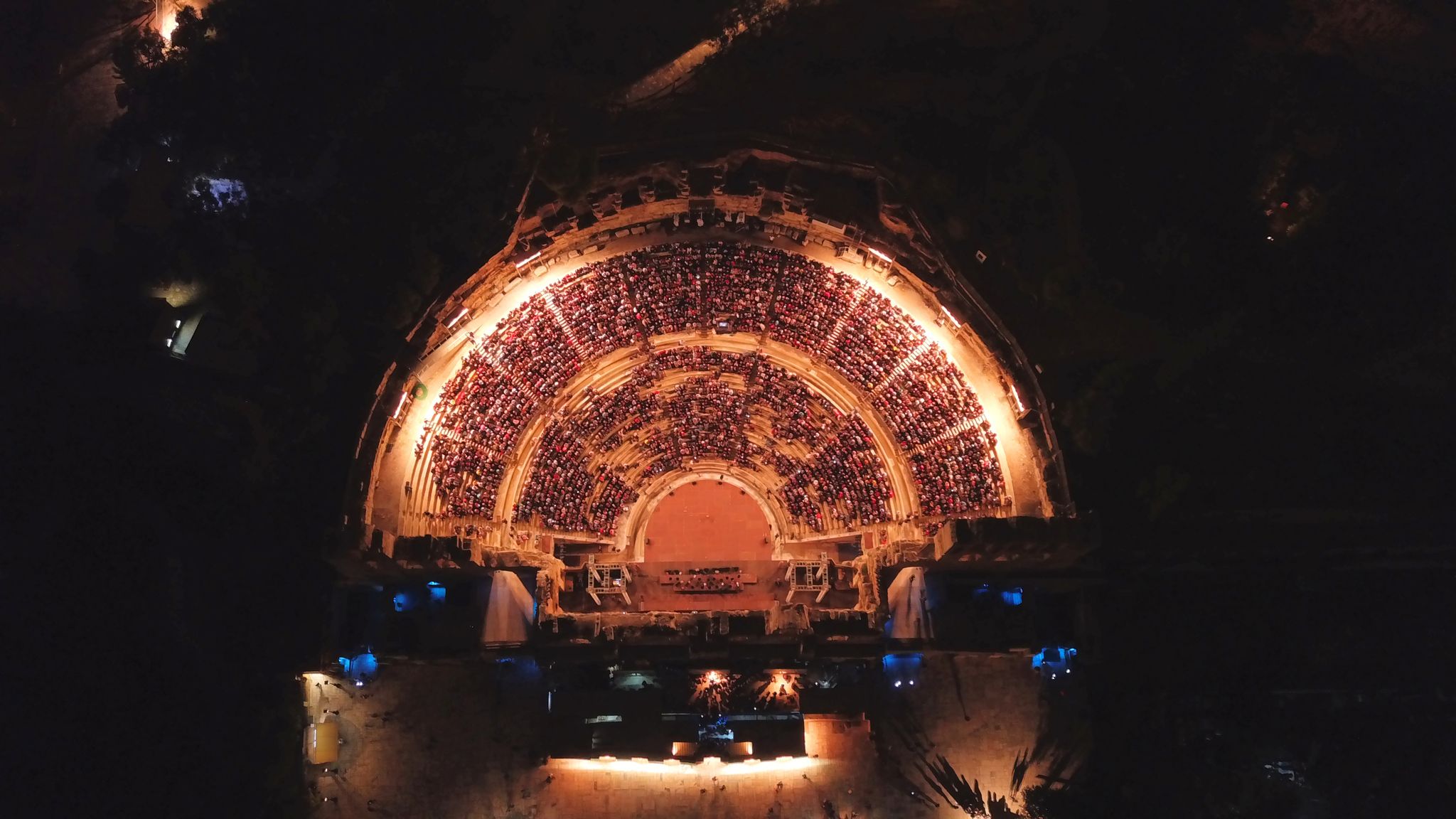 Photo of aerial birds eye view night shot taken by drone of iconic Odeon of Herodes Atticus full of people attending a concert, Athens historic center, Attica, Greece.