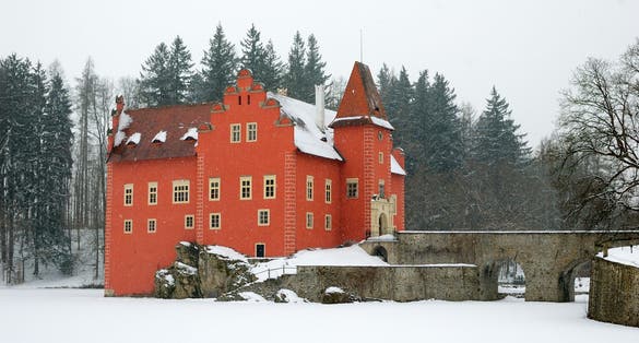 Photo of castle Cervena Lhota in winter, red château standing at the middle of a lake on a rocky island, Czech Republic.