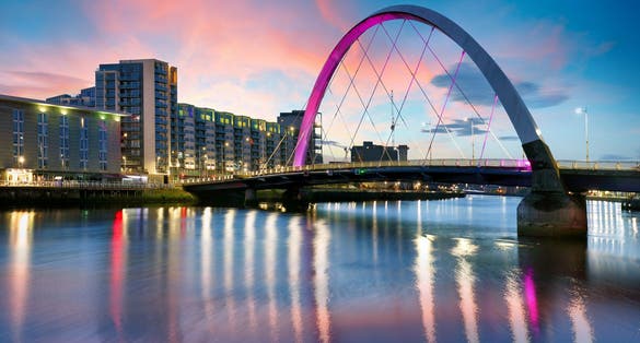 photo of view of Beautiful Sunset Clyde Arc Bridge across river in Glasgow, Scotland, UK. It is nice weather with reflection on water, blue sky, lights from buildings in downtown, skyline, attractions.