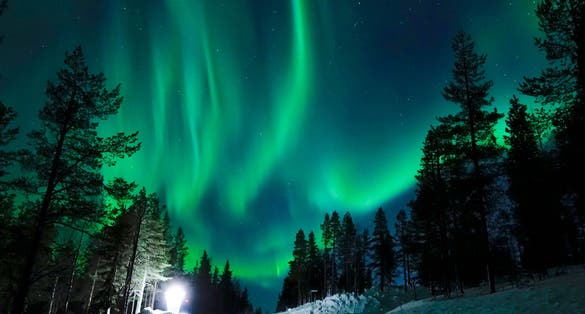 Photo of the northern lights appear above the idyllic Scandinavian countryside in the winter, Rovaniemi, Finland.