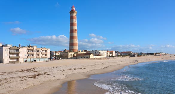 happy senior woman cycling below the navigation sign and ligthouse of Barra at the harbor entrance of Aveiro, Portugal